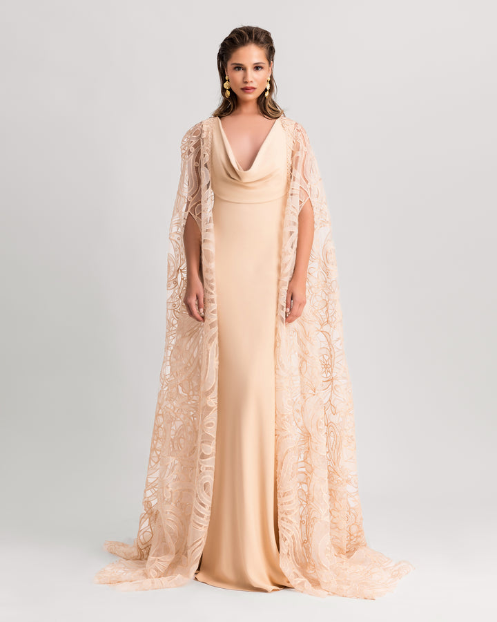 A cowl neckline beige evening dress, paired with a wide patterned  lace cape.