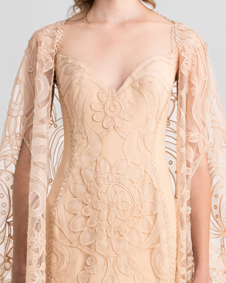 A close-up of a v-neckline, slim-cut lace evening dress in beige color, paired with a wide lace cape.