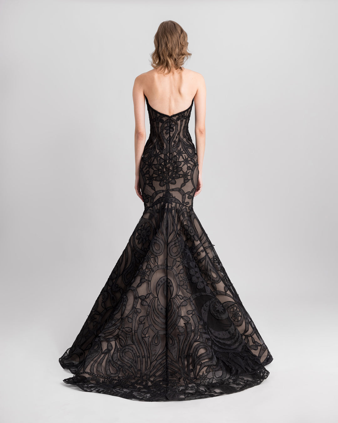 The back of a strapless mermaid-cut lace black evening dress with a flared tail.