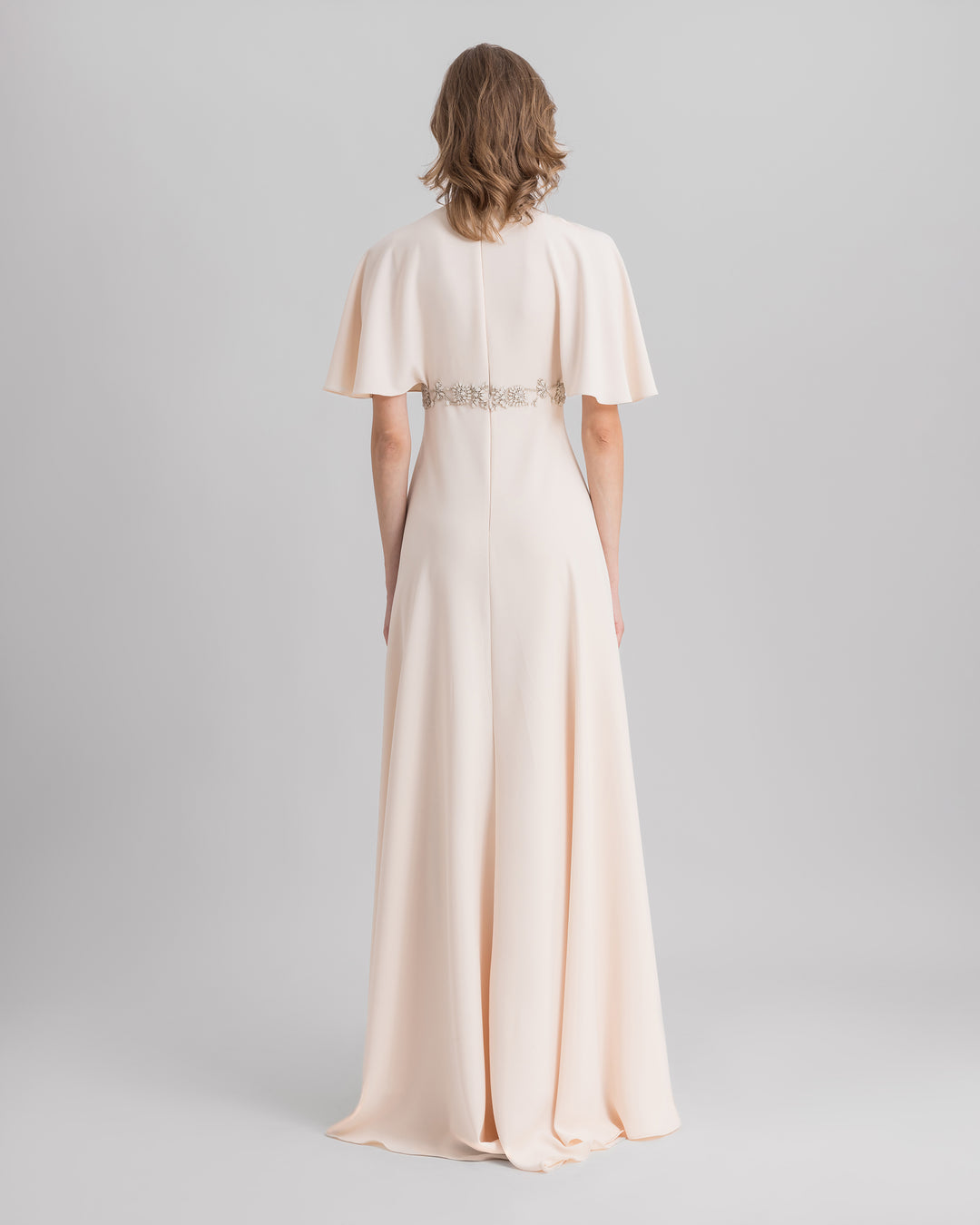 The back of a cream evening dress, featuring a beaded belt and flared sleeves.