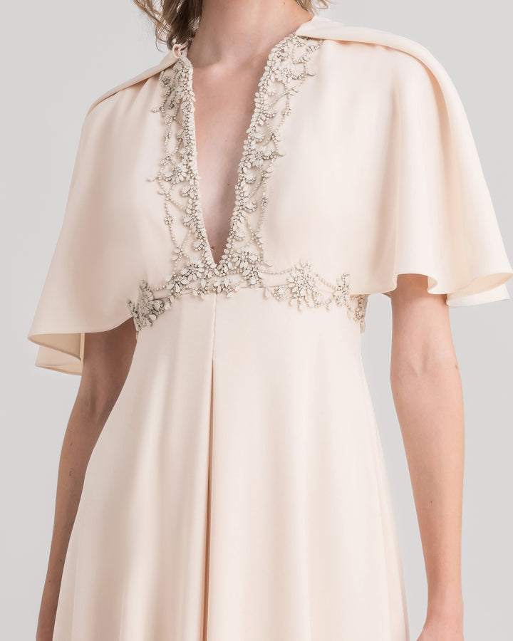 A close-up of a deep beaded v-neckline evening dress in cream, featuring flared sleeves.