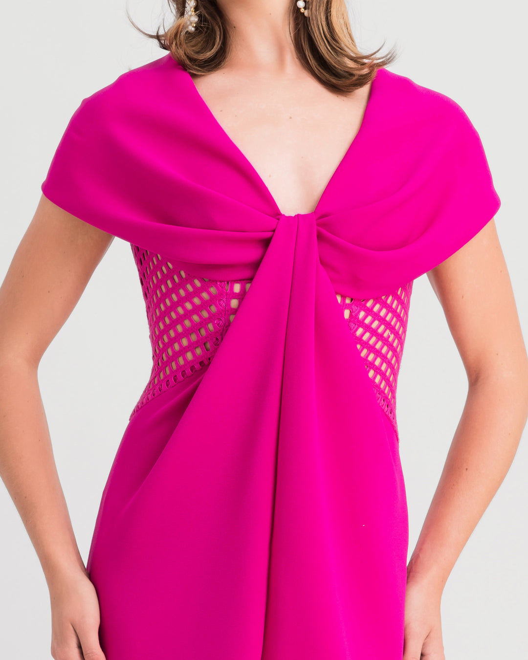 A close-up of a v-neckline fuchsia evening dress with draped bow-like shoulders and crochet lace sides.