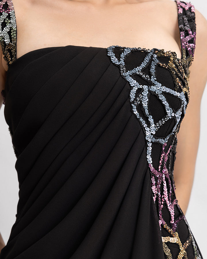 A close-up of a long black evening dress with draping and multicolor beading details.