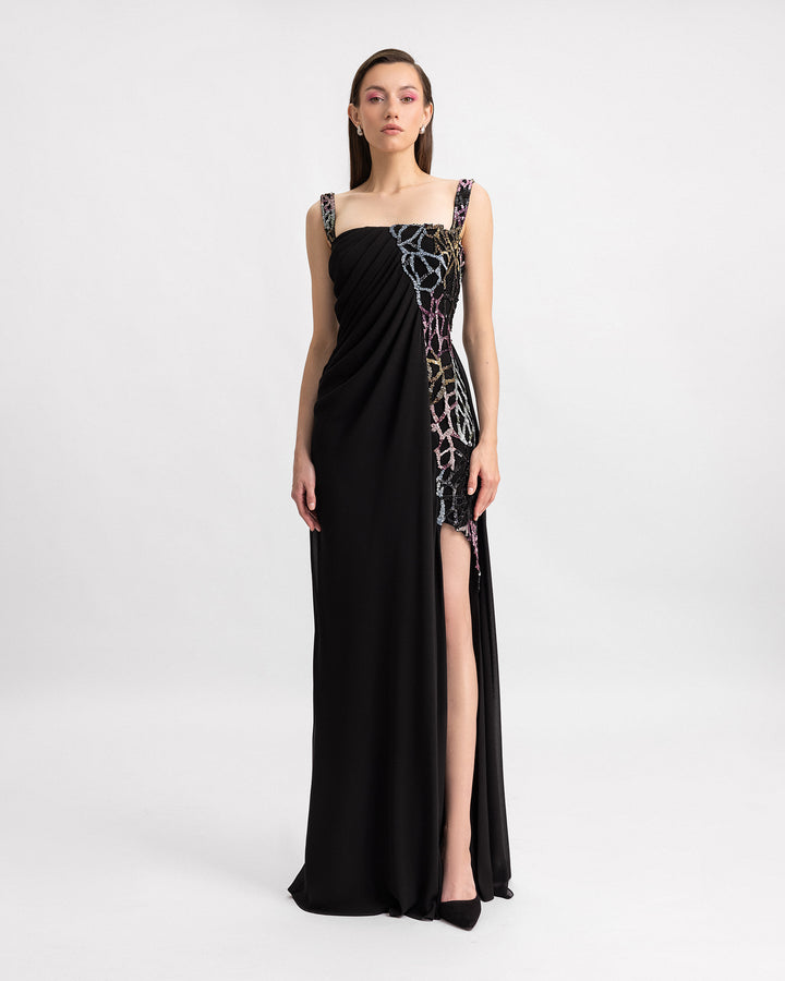 A long black evening dress with draping, multicolor beading details, and a slit on the side.