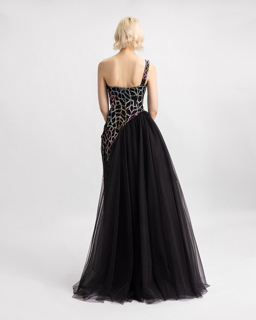 The back of a one-shoulder beaded black evening dress with an asymmetrical tulle skirt.