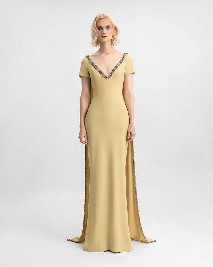 A beaded v-neckline evening dress in golden mustard color with short sleeves and a long cape.