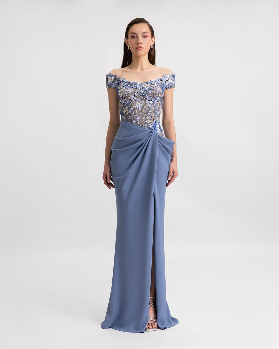 An off-the-shoulders evening dress featuring a beaded corset and a draped skirt with a slit on the side.