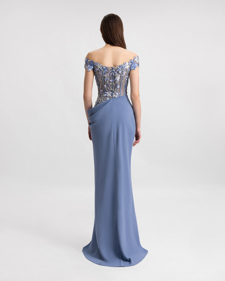 The back of an off-the-shoulders evening dress featuring a beaded corset and a draped skirt with a slit on the side.