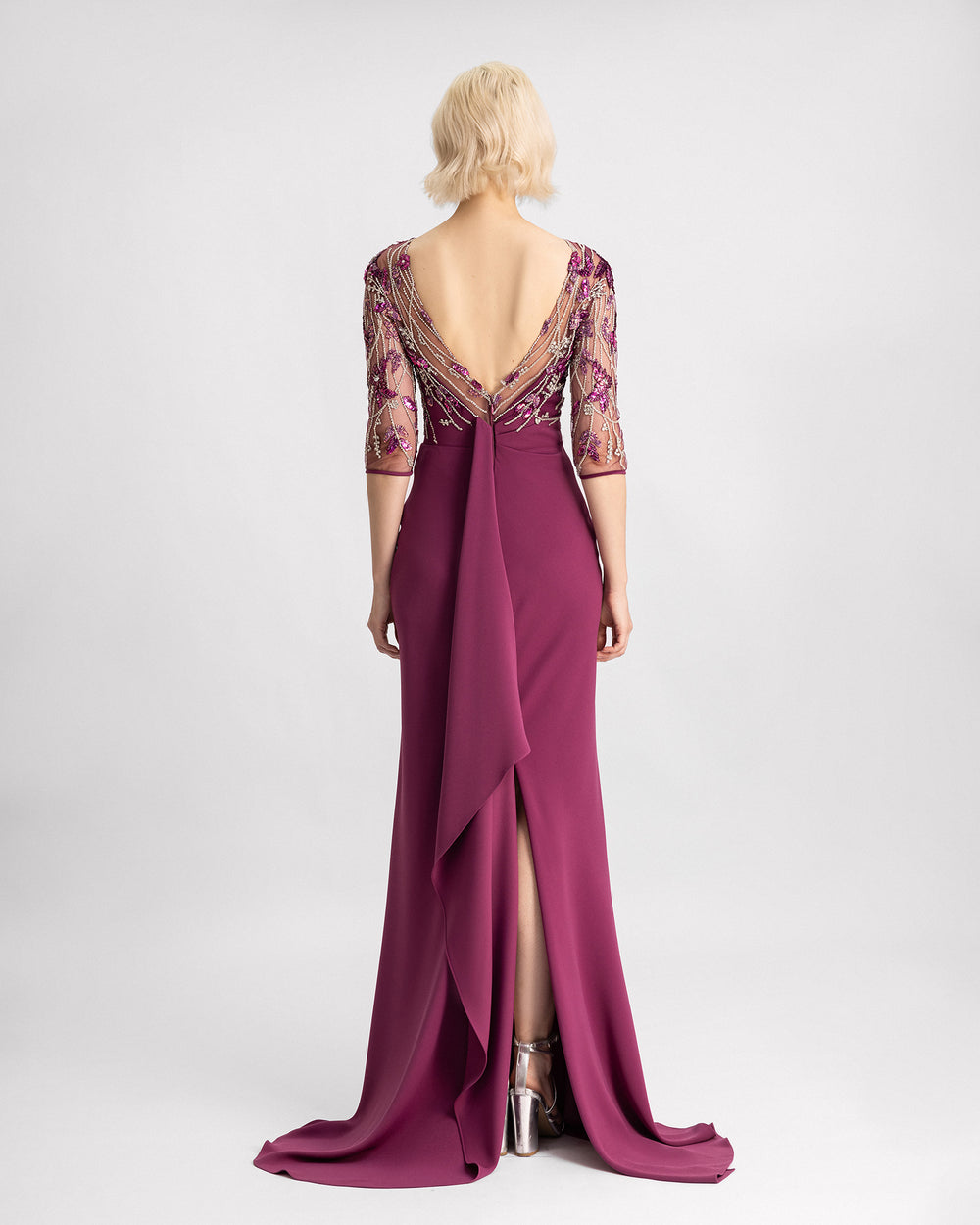 The back of a slim-cut evening dress in mulberry color with a beaded corset, three-quarter sleeves, and a slit at the back.