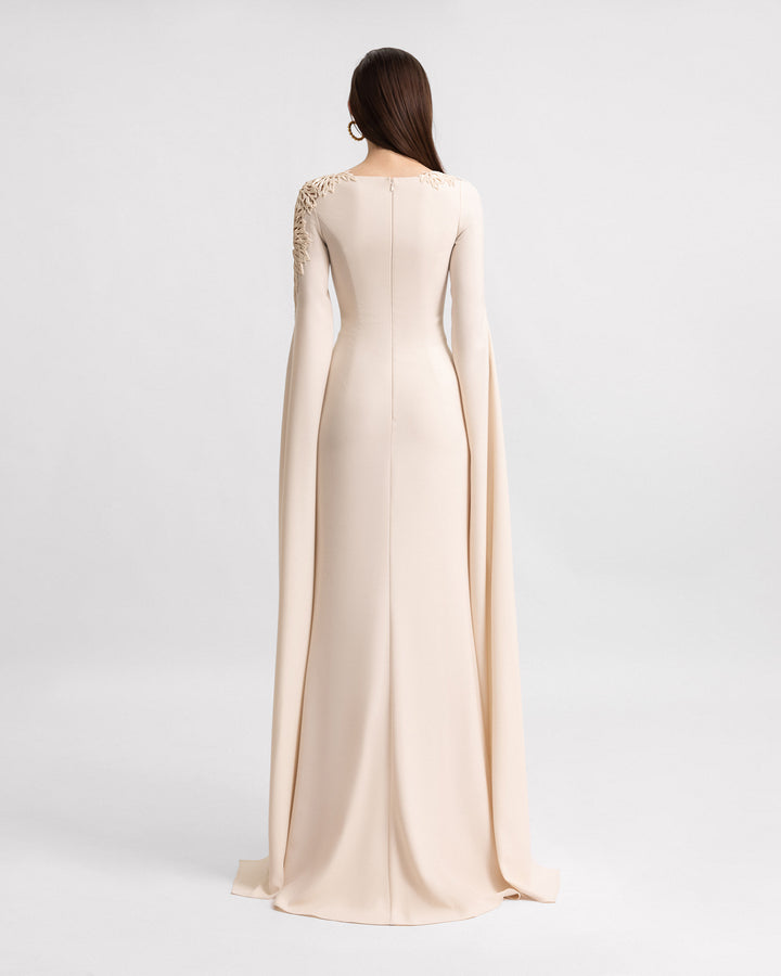 The back of a slim-cut evening dress in champagne color with beadings on the neckline and floor-length sleeves.