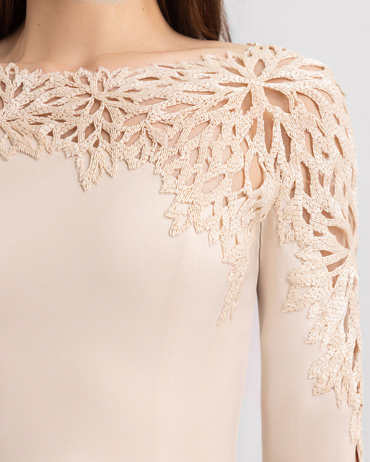 A close-up of a slim-cut evening dress in champagne color with beadings on the neckline and floor-length sleeves.