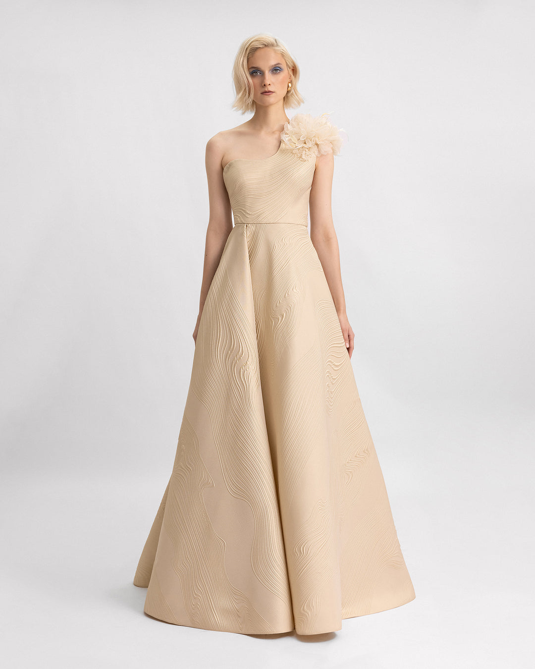 A one-shoulder evening dress in beige jacquard with 3D flowers on the shoulder and a draped full skirt.