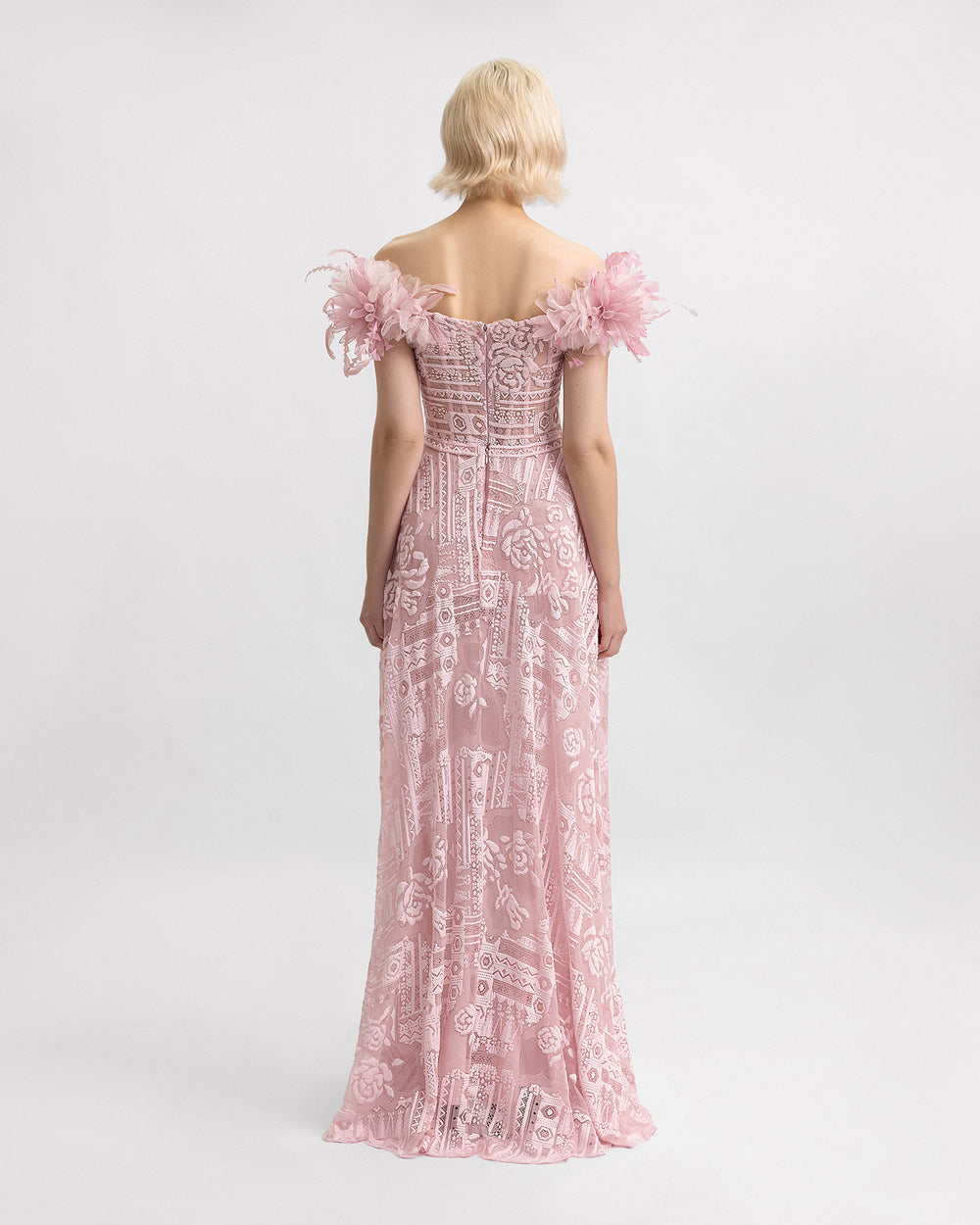 The back of an off-the-shoulders pink lace evening dress with 3D flowers on the shoulders and a structured underskirt.