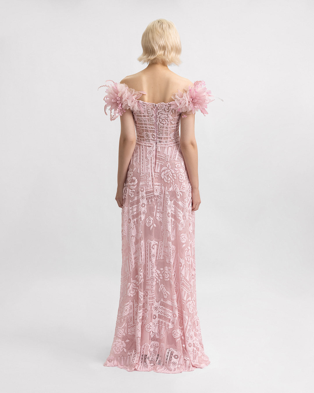 The back of an off-the-shoulders pink lace evening dress with 3D flowers on the shoulders and a structured underskirt.