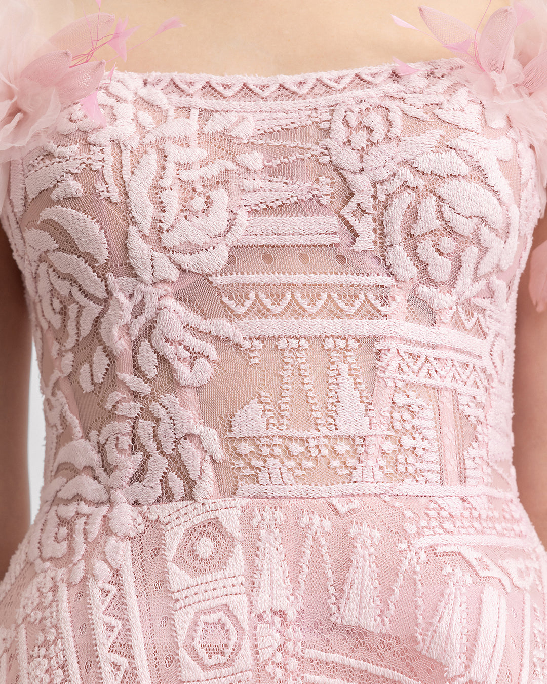 A close-up of an off-the-shoulders pink lace evening dress with 3D flowers on the shoulders and a structured underskirt.