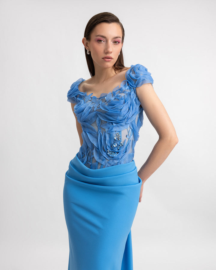 A close-up of a slim-cut blue evening dress featuring a floral embroidered corset and a draped skirt.