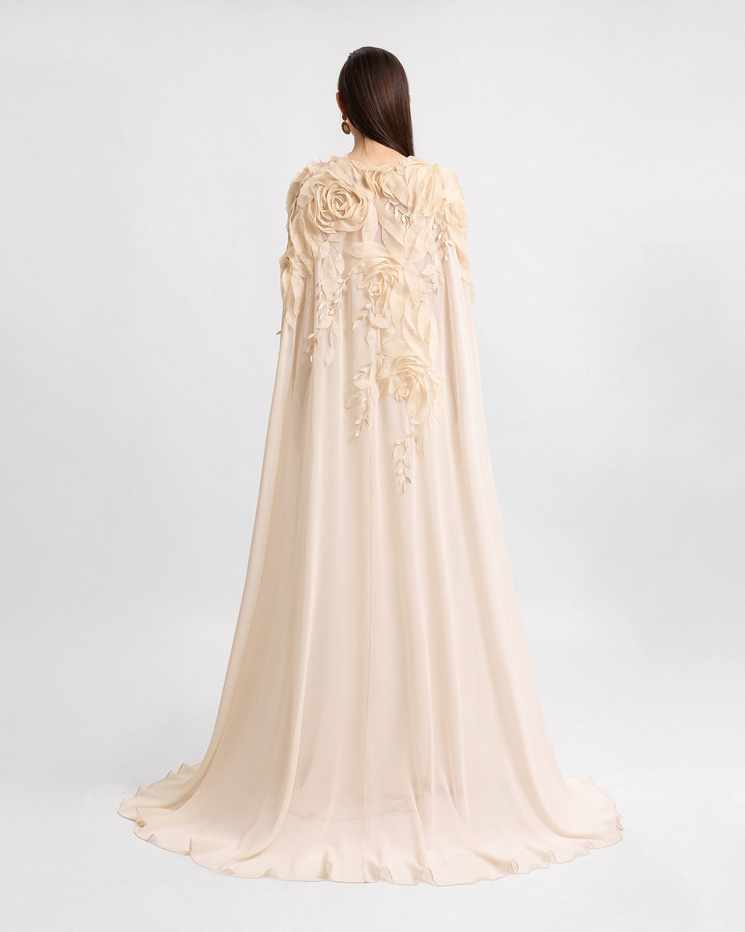 The back of a slim-cut champagne evening dress with floral details, paired with a long cape with embroidered organza flowers.