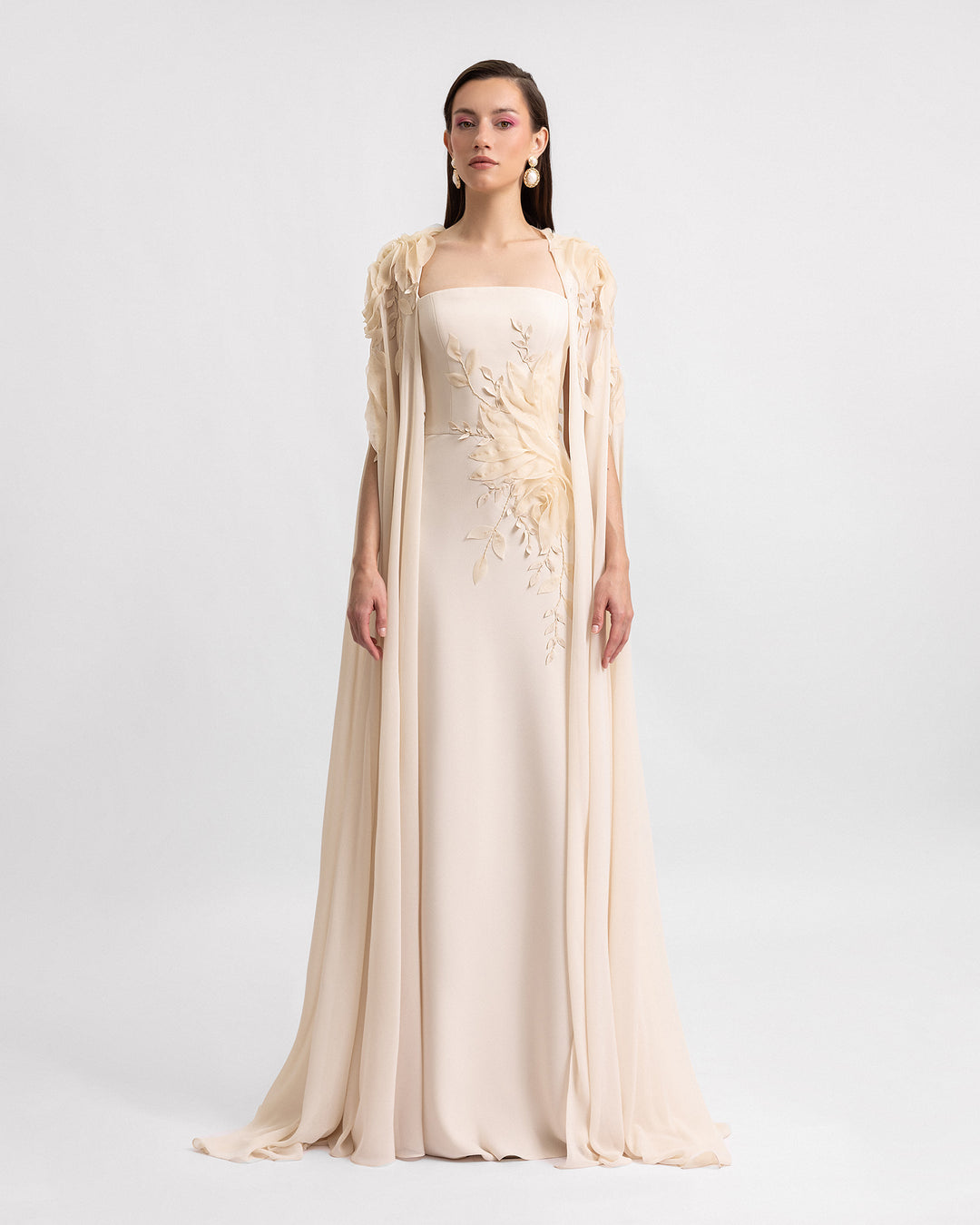 A slim-cut champagne evening dress with floral details, paired with a long cape with embroidered organza flowers.