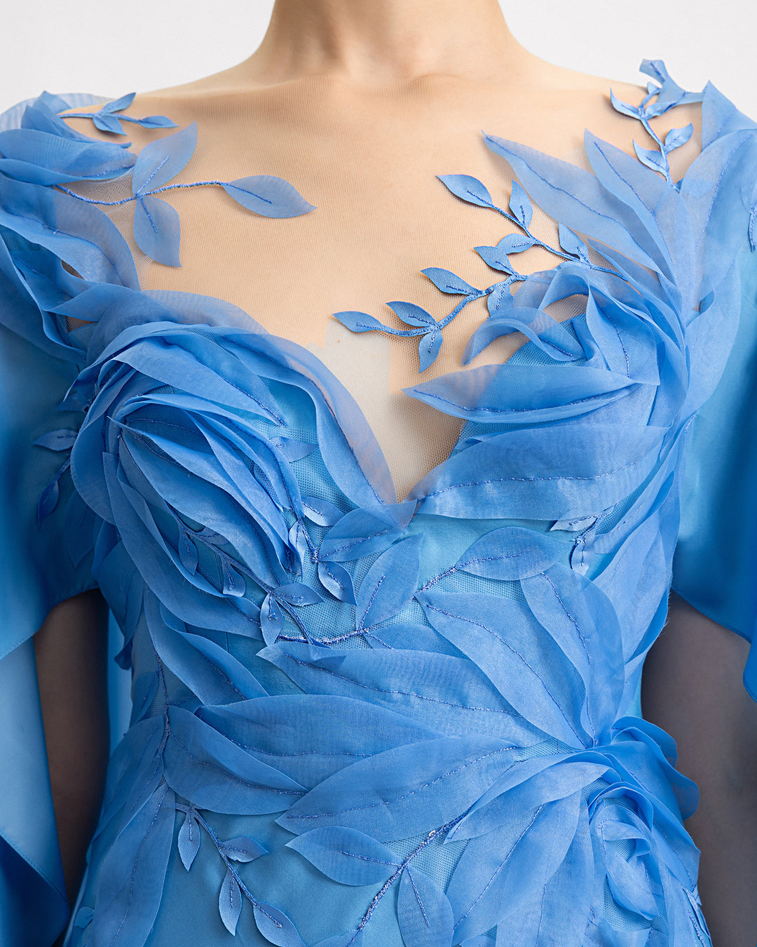 A close-up of a v-neckline silk chiffon dress in blue color with floral embroidered organza details.