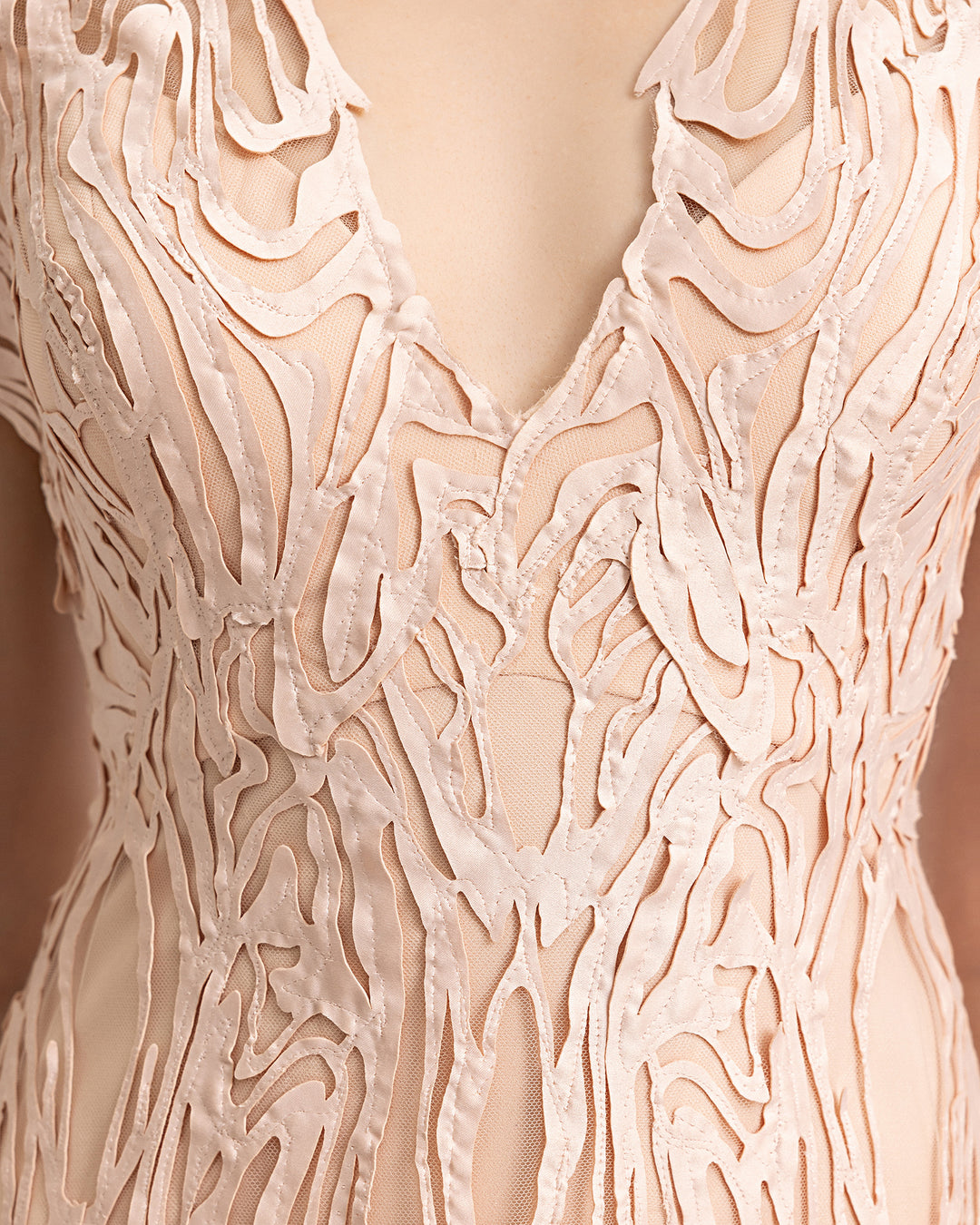 A close-up of a v-neckline evening dress in embroidered laser-cut fabric.