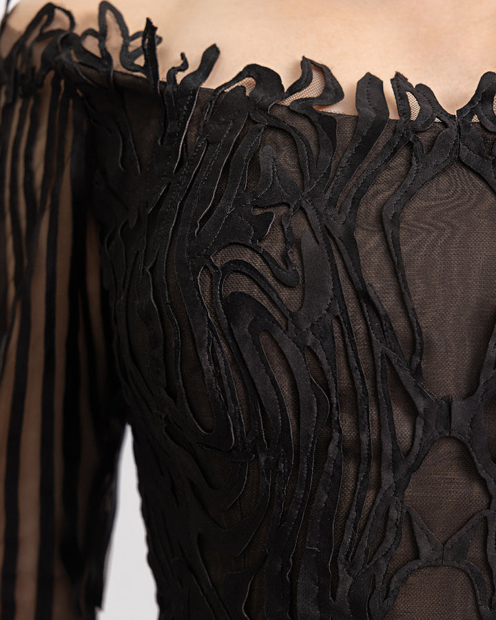 A close-up of an off-the-shoulders black evening dress in a laser cut embroidery fabric.