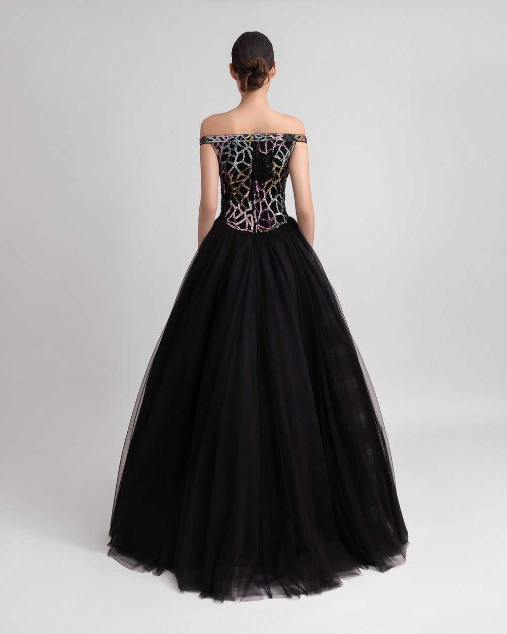 The back of an off-the-shoulder multicolor beaded black evening dress complemented by a dramatic black tulle overskirt at the back.