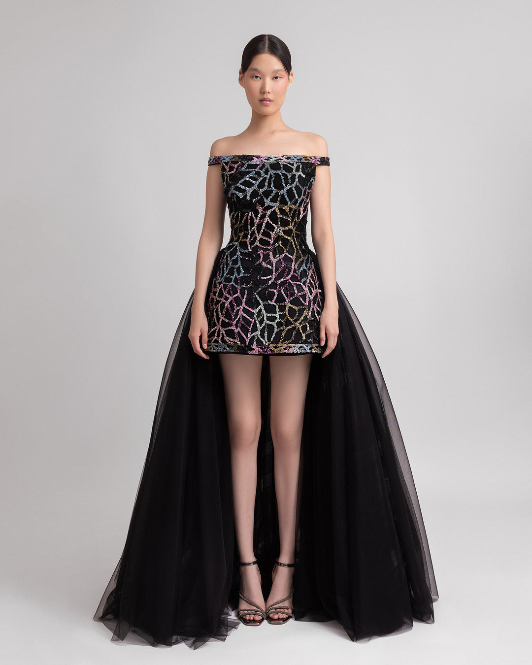 An off-the-shoulder multicolor beaded black evening dress complemented by a dramatic black tulle overskirt at the back.