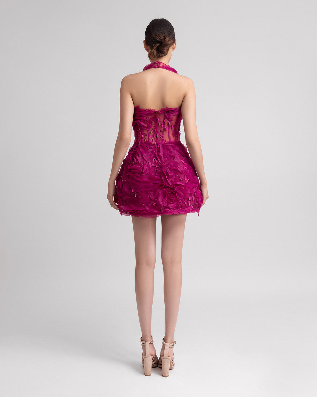 The back of a halter neckline evening dress with a fitted bodice adorned by organza floral appliqués with a structured voluminous skirt and an open back.