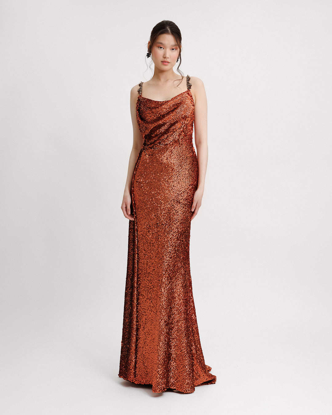 A long fully sequined evening dress in copper color with a draped corset and beaded straps.