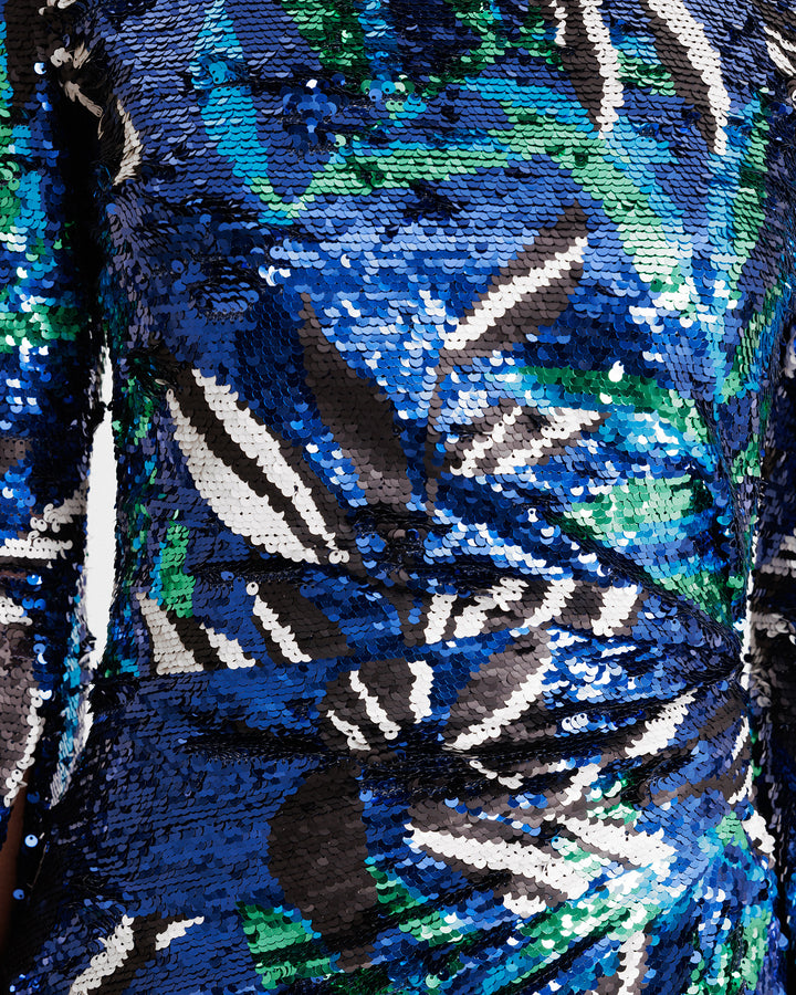 A close-up of a slim-cut evening dress featuring draping on the waist in a patterned sequins fabric.