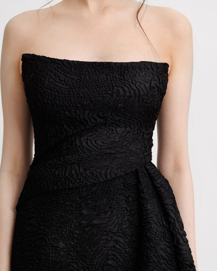 A close-up of a strapless black dress with a one-sided waist draping.