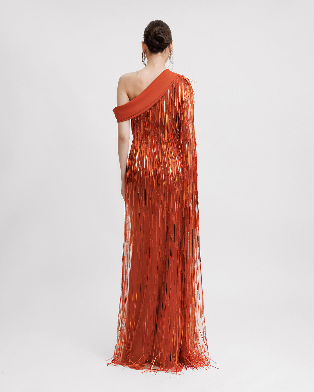 The back of a fully beaded fringe evening dress in orange color featuring a one-shoulder crepe fold-over, and a single floor-length sleeve.