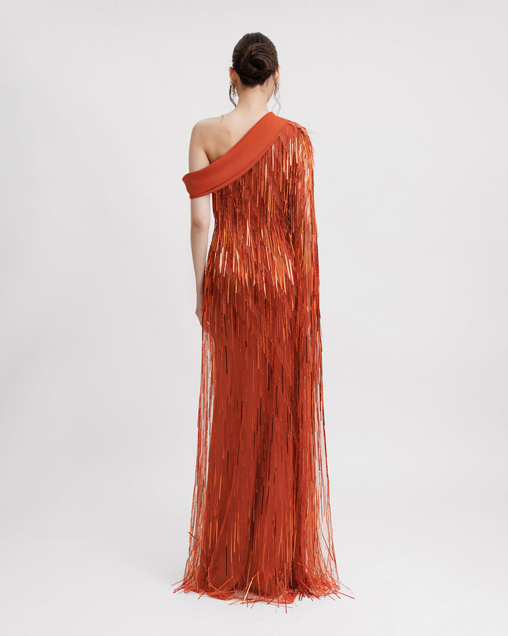 The back of a fully beaded fringe evening dress in orange color featuring a one-shoulder crepe fold-over, and a single floor-length sleeve.