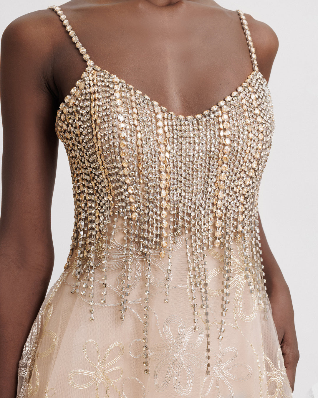 A close-up of an evening dress with beaded tassels and a flared embroidered champagne skirt.