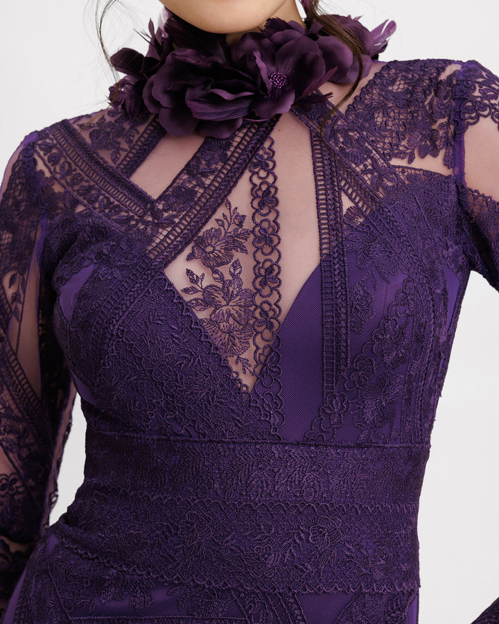 A close-up of a long sleeved evening dress in purple patterned lace fabric, featuring a see-through plunging neckline and embroidered floral feathers on the collar.