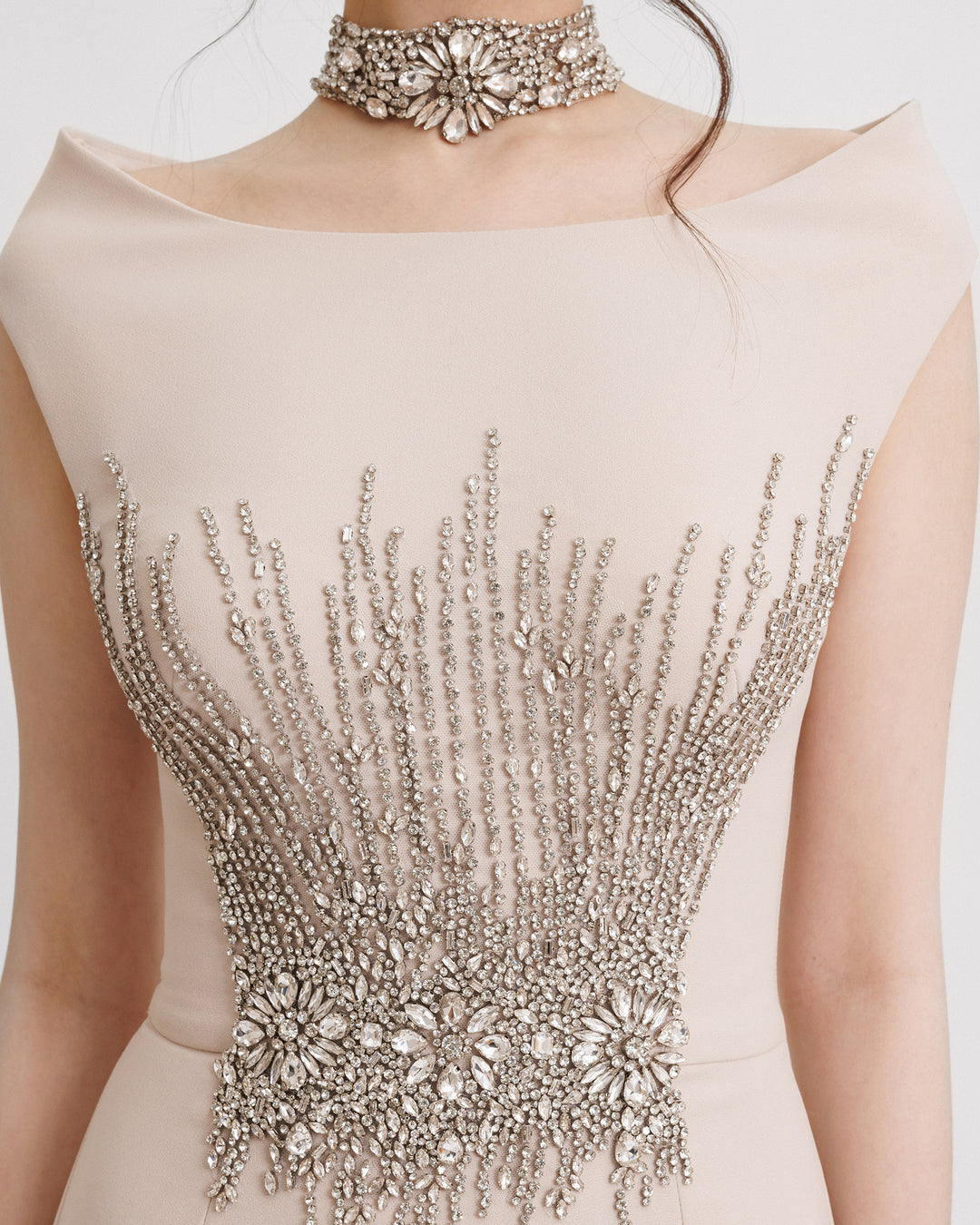 A close-up of a slim-cut champagne evening dress featuring a strapless boat neckline with a detachable collar and beadings on the corset