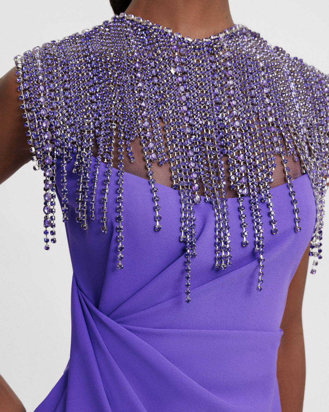 A close-p of a slim-cut purple evening dress with a beaded tassels collar, and draping on the waist.