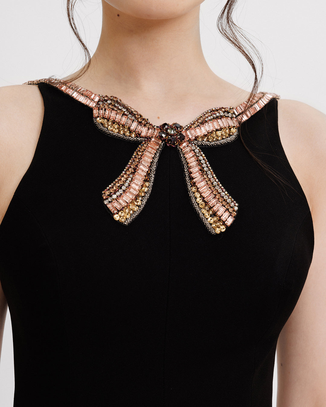 A close-up of a slim-cut black evening dress featuring a beaded bow at the collar.