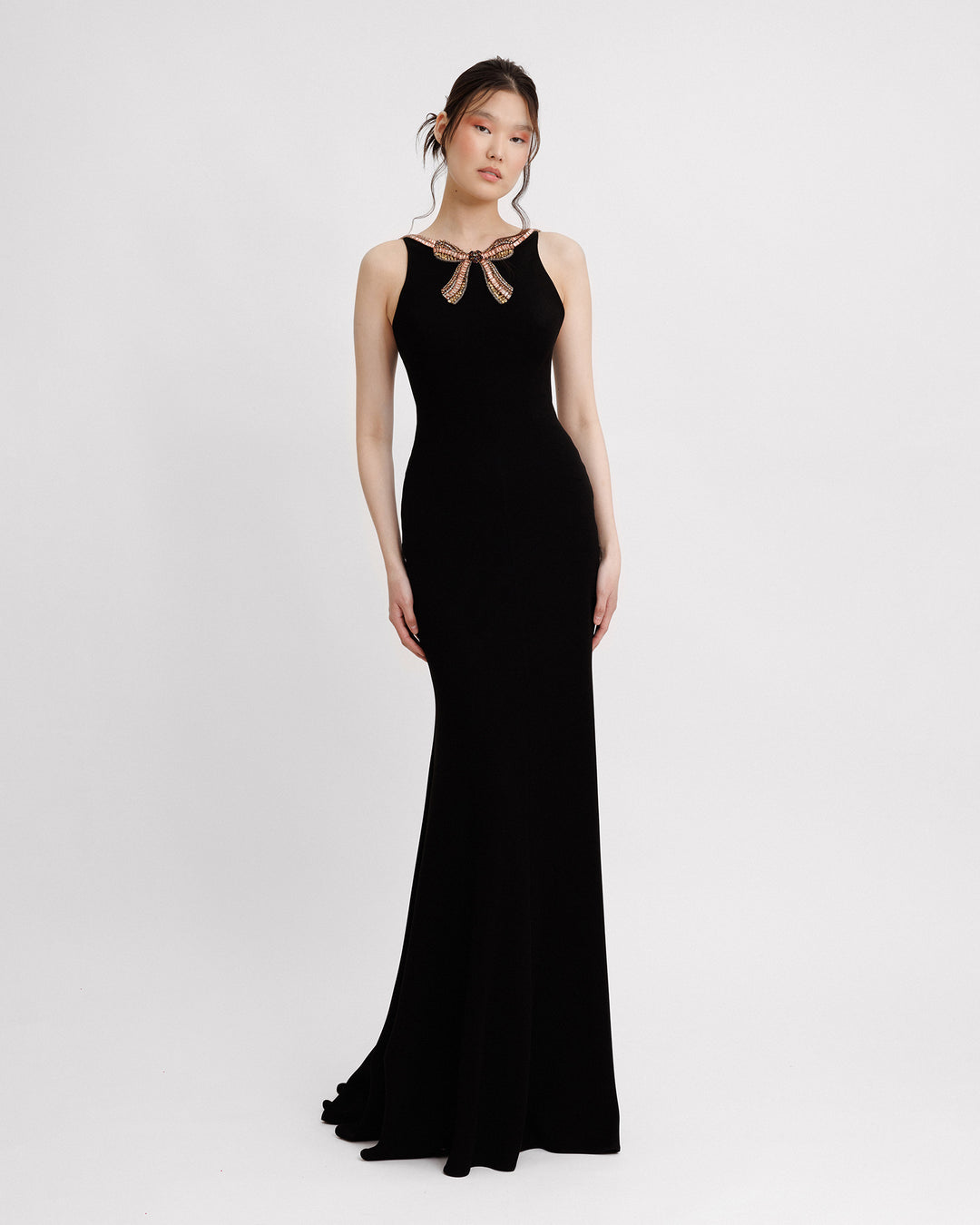 A long slim-cut black dress featuring a beaded bow at the collar.