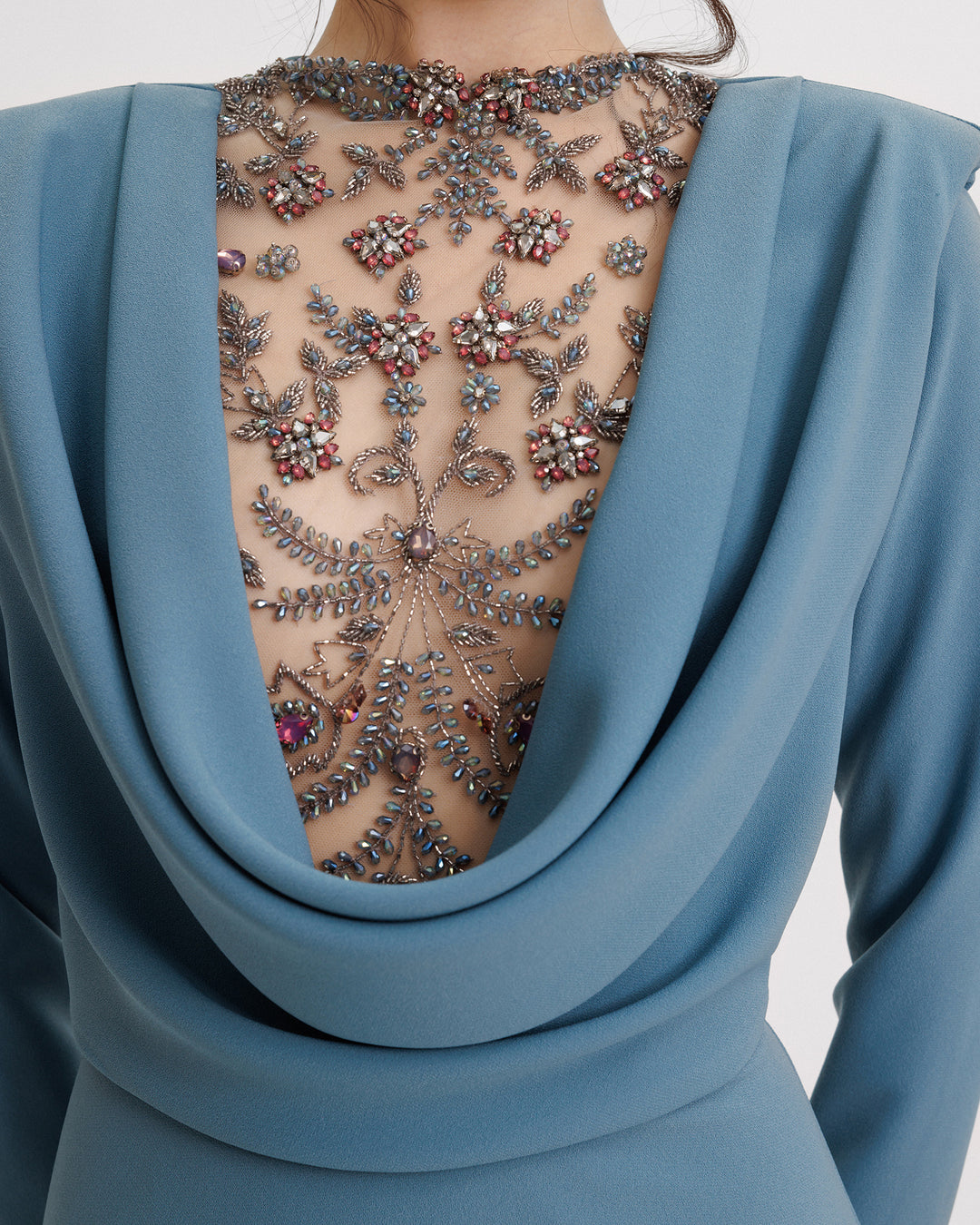 A close-up of a a long sleeves slim-cut evening dress featuring a beaded cowl-neckline with draping and structured shoulders.