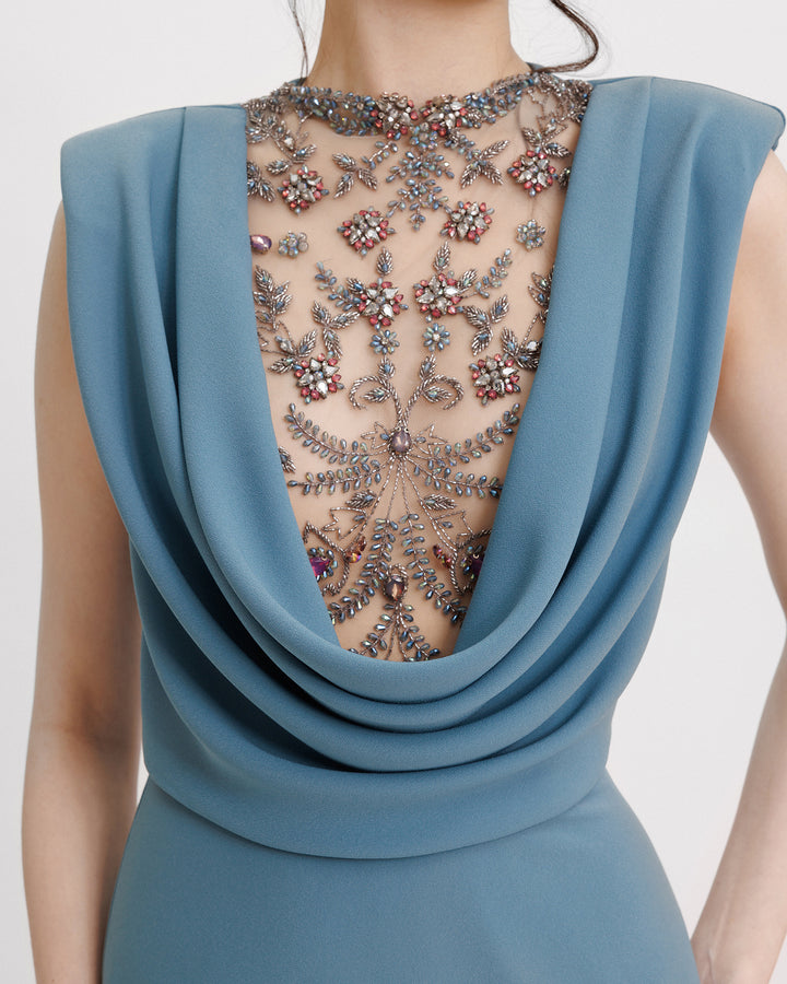 A close-up of a slim-cut blue evening dress featuring a beaded cowl-neckline and structured shoulders.