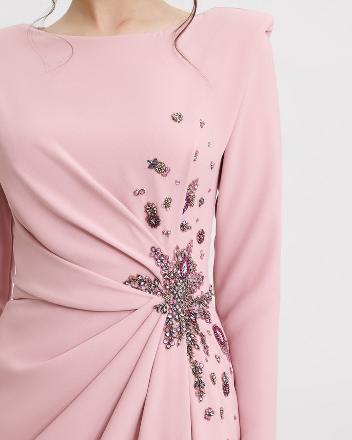 A close-up of a long sleeved slim-cut evening dress in pink color featuring structured shoulders, draping and floral beadings on the waist.