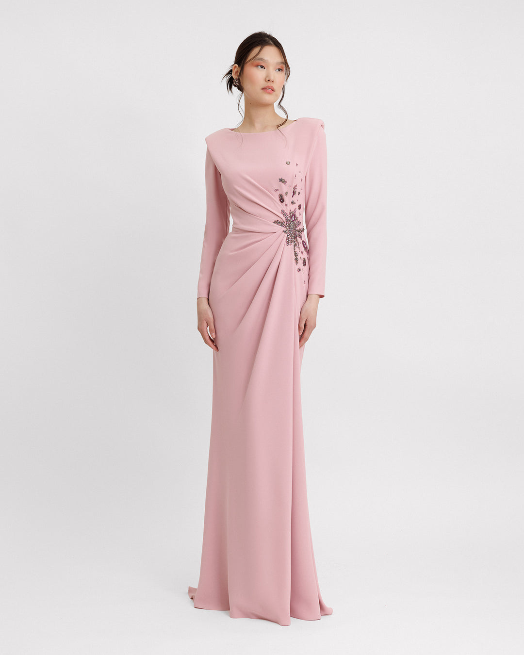 A long sleeved slim-cut evening dress in pink color featuring structured shoulders, draping and floral beadings on the waist.