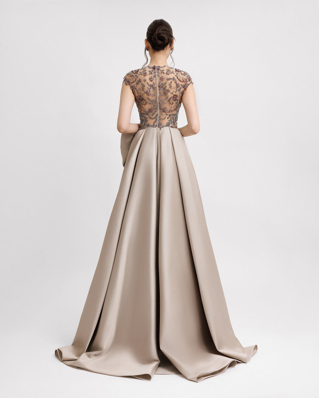 The back of a long evening dress featuring a fully beaded see-through back and a wide draped mikado skirt.