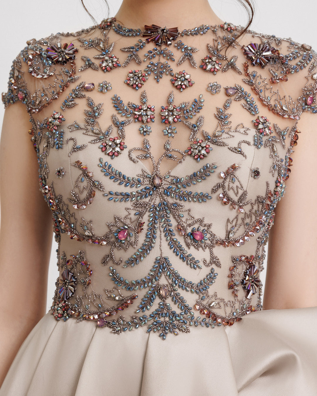 A close-up of a long evening dress featuring a fully beaded corset and a draped mikado skirt in greige color.