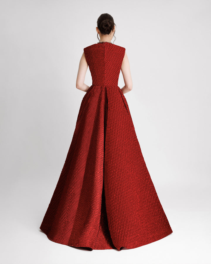 The back of an embellished V-neckline evening dress with structured shoulders and a draped flared skirt in red crinkled jacquard fabric.