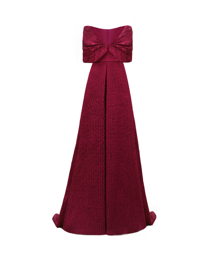 A dark fuchsia strapless evening dress with a plunging neckline and draping on the waistline, paired with a detachable bow-like cape.