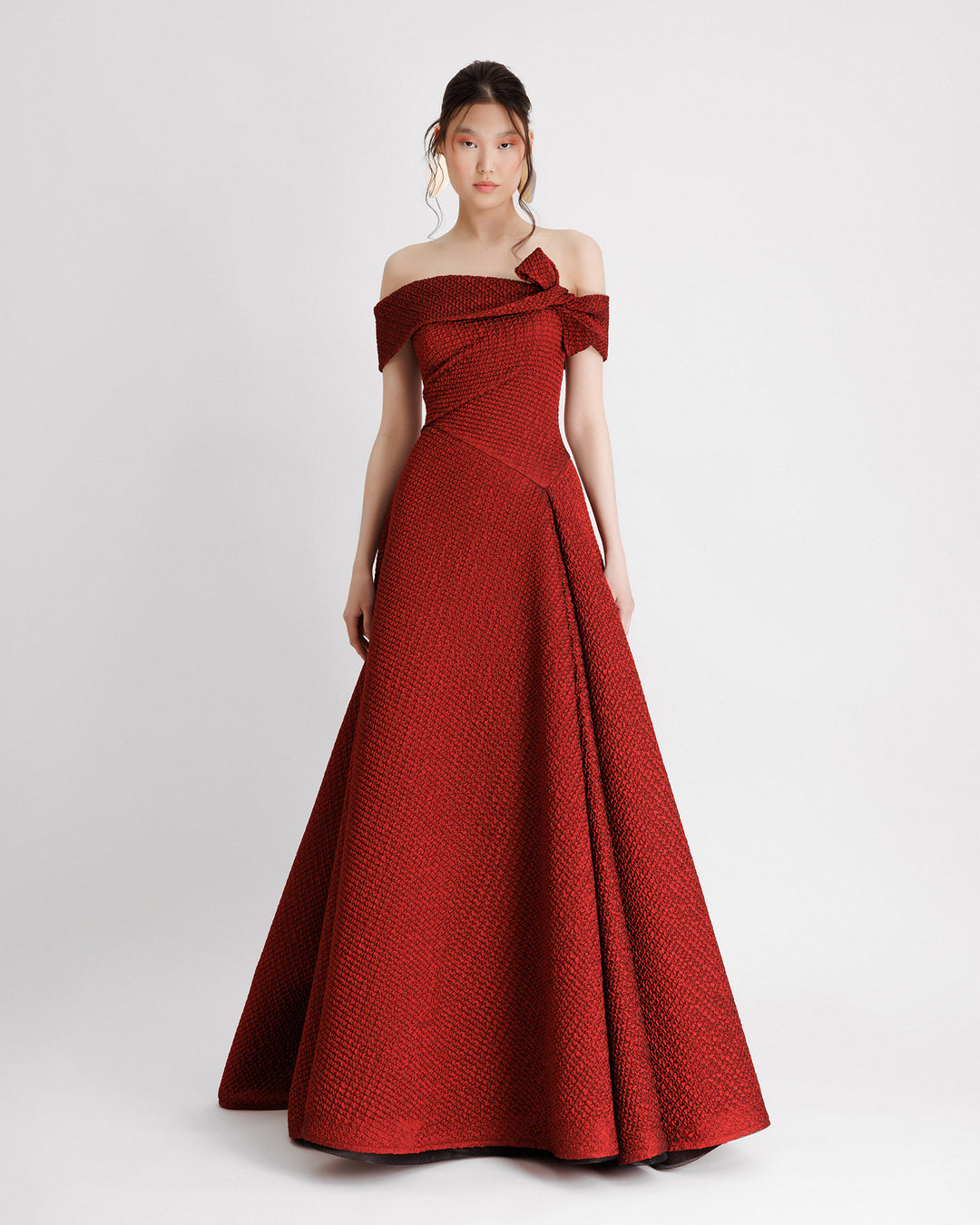 An off-the-shoulders red evening dress with an asymmetrical waistline and draped flared skirt.