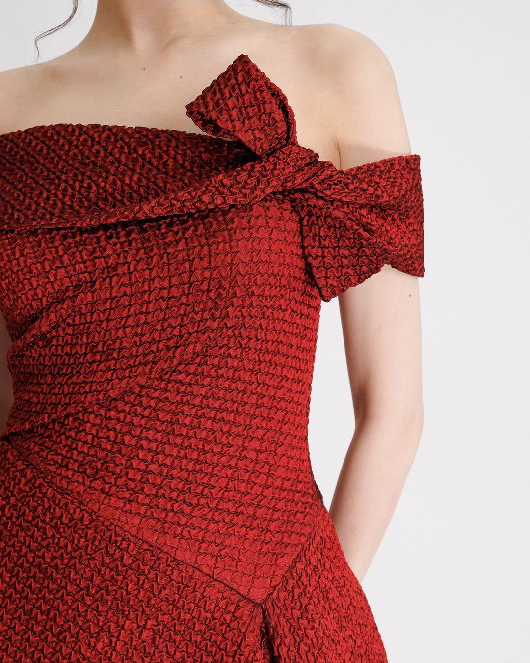 A close-up of an off-the-shoulders red evening dress with an asymmetrical waistline.