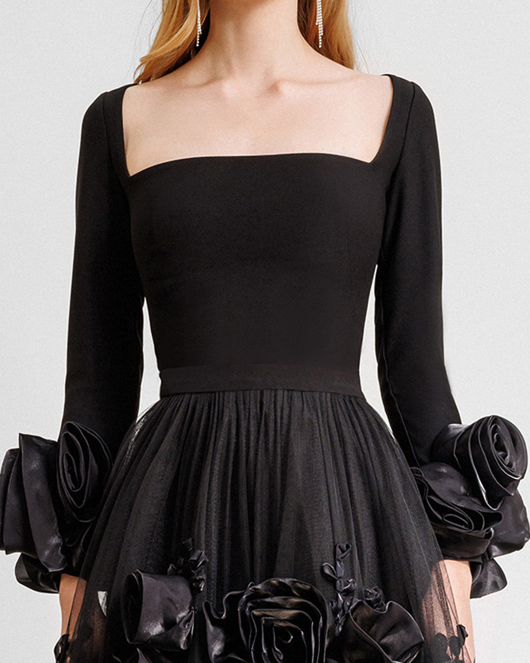 A close-up of a black evening dress featuring a squared-neckline crepe top gathered with a midi tulle skirt adorned with floral cuffs and and embellishments on the skirt.